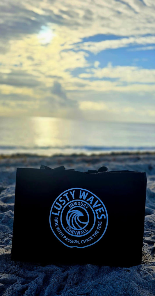 Black bag with 'Lusty Waves' logo on a beach with ocean and sky in the background